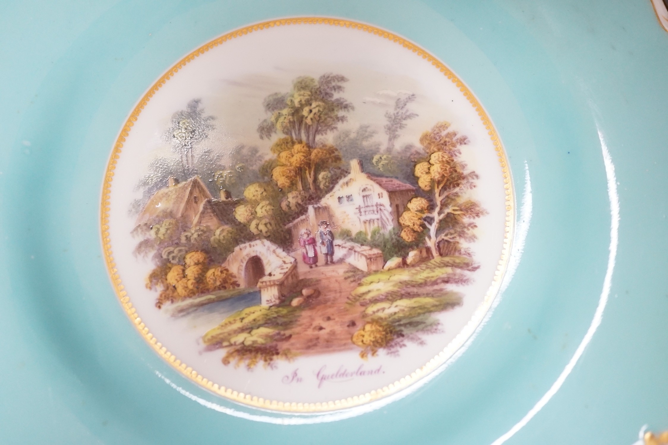 A pair of English porcelain plates with moulded white and turquoise borders both painted with landscapes, one titled in Guildford, diameter 22.5cm
